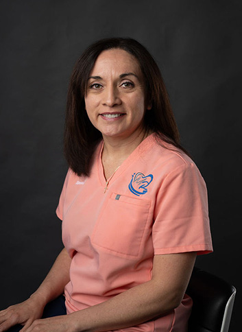 A woman wearing a pink scrub top with a badge on her left side, smiling at the camera.